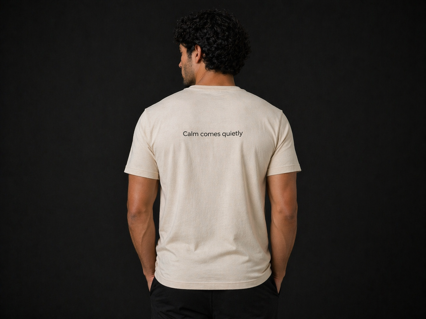 Male model wearing Quiet Tide minimalist t-shirt in natural color with back logo on dark luxury background