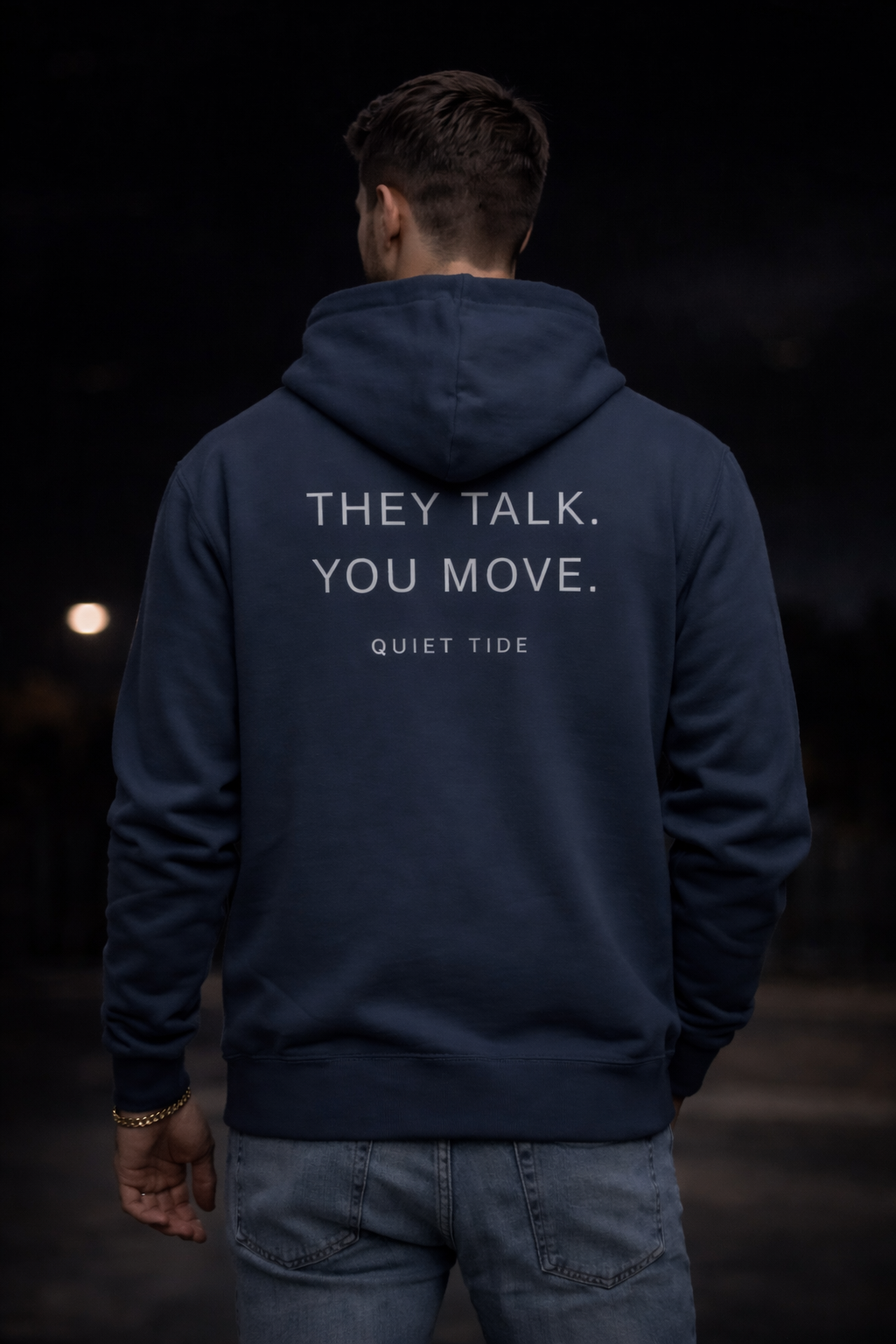 Man wearing Quiet Tide Indian Ink Grey (dark grey) hoodie back view with “They Talk. You Move.” text