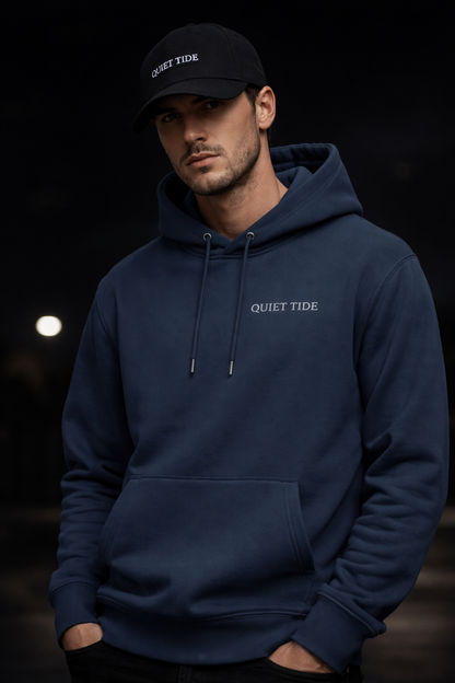 Man wearing Quiet Tide Indian Ink Grey hoodie with minimal chest logo against dark background
