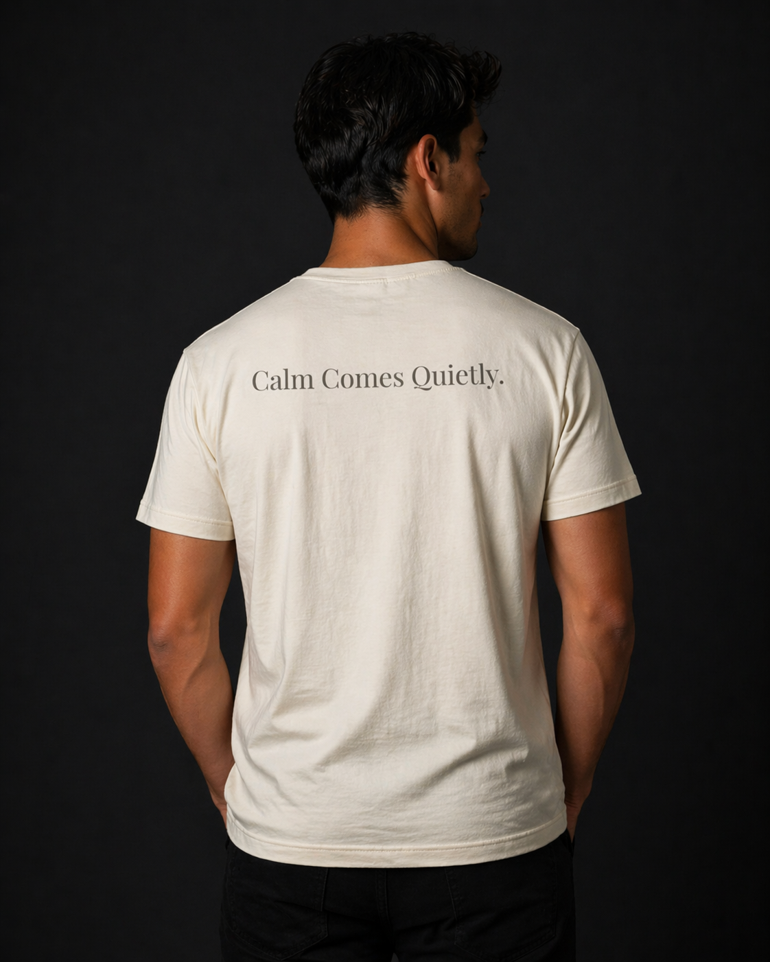 Man wearing Quiet Tide natural t-shirt back view with “Calm Comes Quietly” text on black background